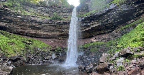 The two-tiered Kaaterskill Falls in the Catskills drops over a rocky cliff into a pool surrounded by greenery.