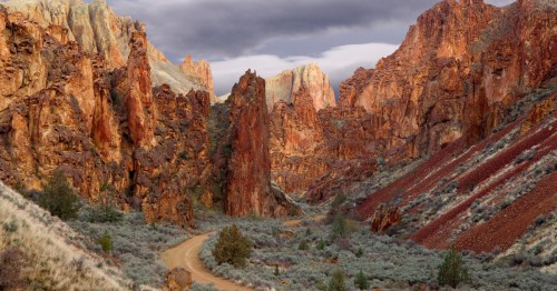 A dirt road winds through a desert landscape toward massive rock formations in eastern Oregon.