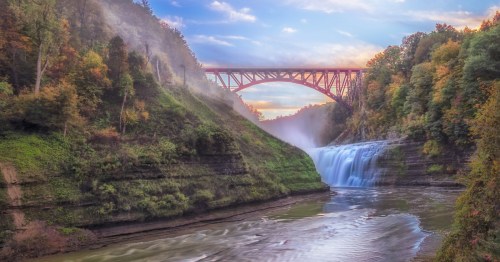 Letchworth State Park Middle Falls and historic steel railroad bridge in a misty gorge during a colorful sunrise.