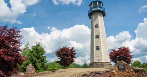 A lighthouse and memorial plaque in a clearing on a hill.