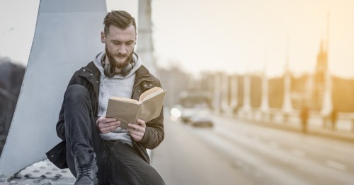 a man wearing a leather coat sitting on a urban bridge reading a book with traffic blurred in the background, the literary destination in Camden, New Jersey