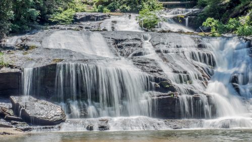 A serene waterfall cascading over rocky terrain, surrounded by lush green trees and foliage.