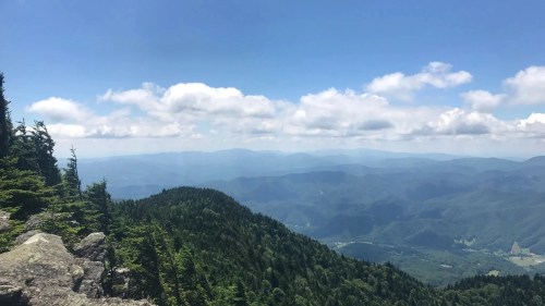 A panoramic view of lush green mountains under a bright blue sky with scattered clouds.