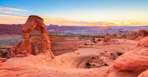Delicate Arch surrounded by red slickrock with a fiery sunset overhead.