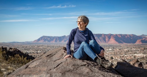an active senior womansits on a rock while hiking in the arizona desert