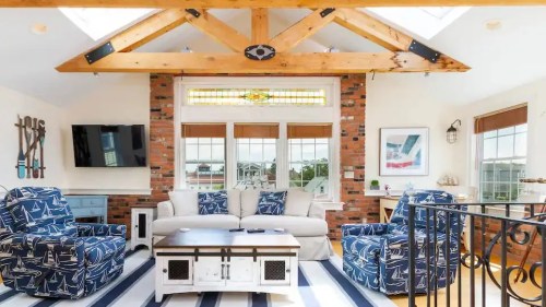 Bright living room with nautical decor, featuring blue patterned chairs, a coffee table, and large windows.