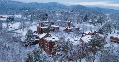 A college campus full of red brick buildings is blanketed by snow with hills in the background.