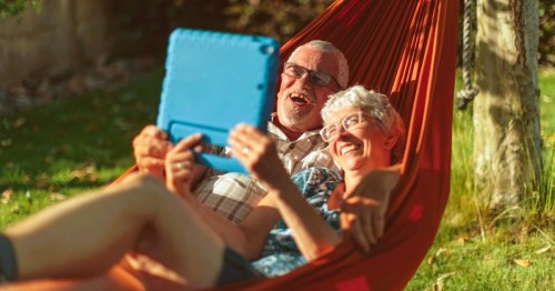 Elderly couple in Alabama, relaxing in a hammock using a tablet while sharing a joyful moment.