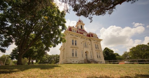 Low angle view of the historic limestone Chase County Courthouse with a red roof under a blue sky in Cottonwood Falls, KS.