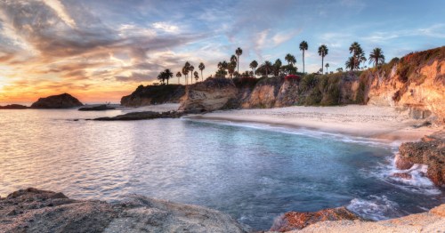 Serene shoreline and glowing cliffs above clear waters at Treasure Island Beach in California at sunset.