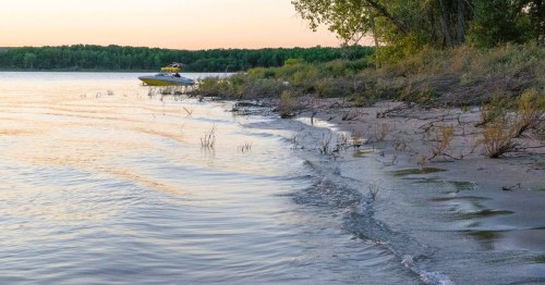 A boat drifting on the crystal-clear waters of Glendo Lake in Wyoming, featuring a sandy beach with gentle waves during sunset.