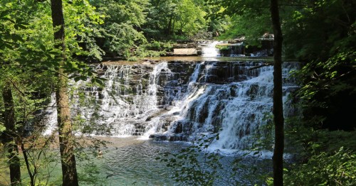 The crystal-clear waters at Rutledge Falls in Tennessee cascade over tiered rocks in a lush green forest.