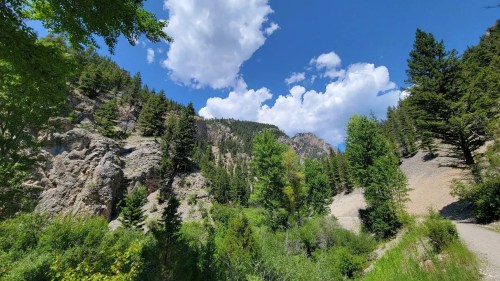 A scenic view of a lush green valley surrounded by mountains under a bright blue sky with fluffy white clouds.