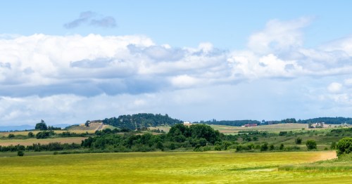 Rolling hills of farmland and small groups of trees stretch out into the distance under a cloudy sky.