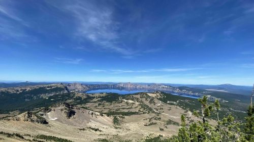 A panoramic view of a mountainous landscape with a lake in the distance under a clear blue sky.