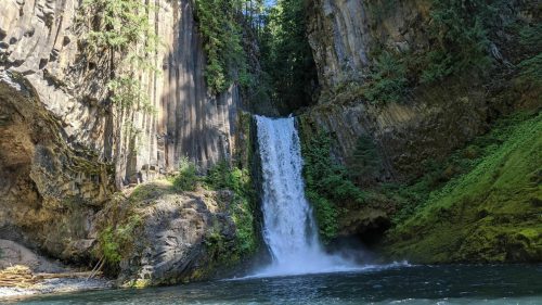 A serene waterfall cascades down rocky cliffs, surrounded by lush greenery and a clear blue pool below.