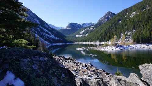 A serene mountain lake surrounded by lush green forests and snow-capped peaks under a clear blue sky.