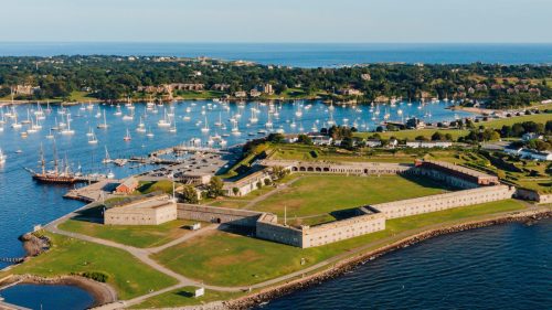 Aerial view of a coastal fort surrounded by green lawns, boats in the harbor, and a clear blue sky.