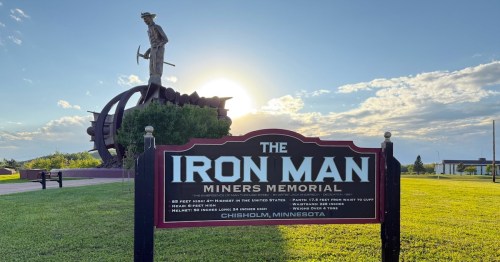 A towering side-profile view of the historic rustic metal miner statue with a pick in Chisholm, Minnesota.