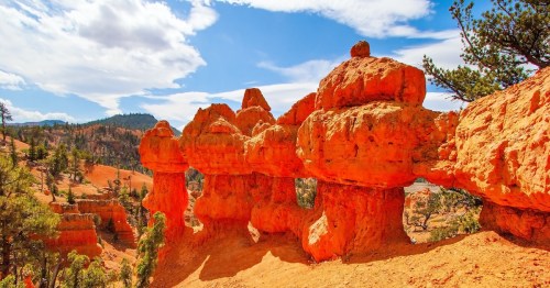 Bright orange natural rock hoodoos and a small rock arch stand against a blue sky at Losee Canyon in Utah.