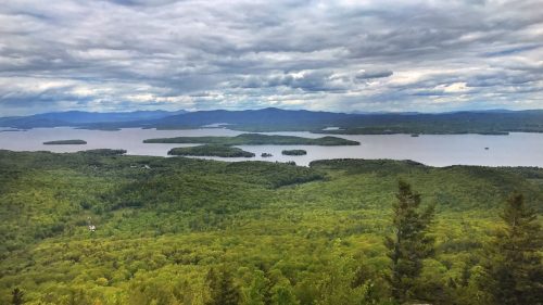 A panoramic view of lush green forests and a lake dotted with islands under a cloudy sky.