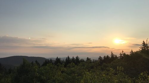A serene sunset over a mountainous landscape, with trees silhouetted against a colorful sky.