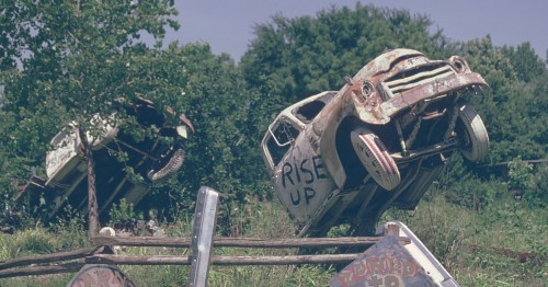 An antique truck upended in concrete featuring the hand-painted "Rise Up" slogan at Truckhenge, Kansas.