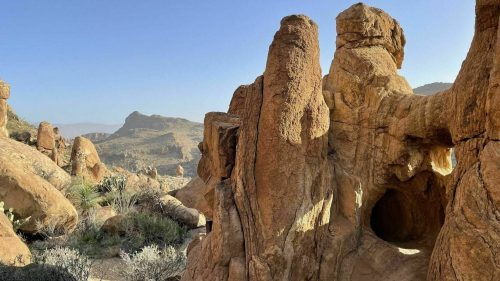 Rocky formations and a cave entrance in a desert landscape under a clear blue sky.