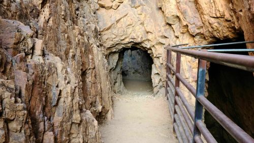 Narrow pathway leading into a rocky cave, with a metal railing along one side.