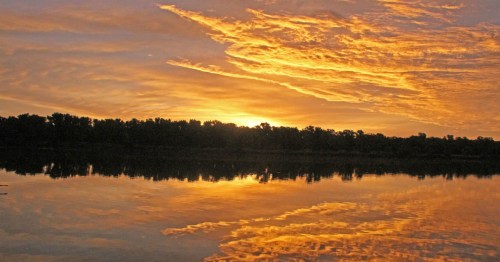Vibrant orange and yellow sunset reflecting perfectly on the still water of Milford Lake, KS.