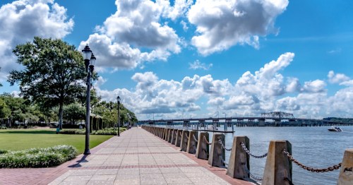 A paved walkway near the riverfront in Beautfort, South Carolina under a beautiful blue sky with puffy white clouds.