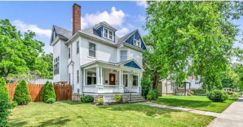 A charming white Victorian-style house with blue gables, a front porch, and a large brick chimney.
