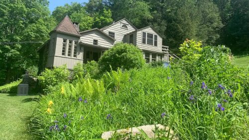 A charming house surrounded by lush greenery and colorful flowers under a clear blue sky.