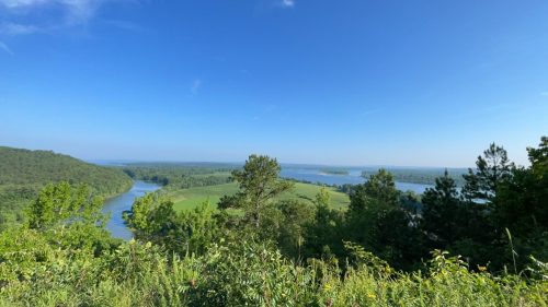 A scenic view of a river winding through lush green landscapes under a clear blue sky.