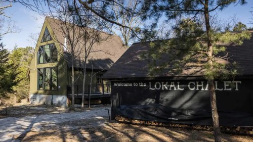 A cozy chalet with a sign reading "Welcome to the Lokal Chalet," surrounded by trees and a clear blue sky.