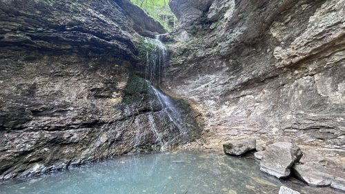 A serene waterfall cascading down rocky cliffs into a clear pool, surrounded by lush greenery.