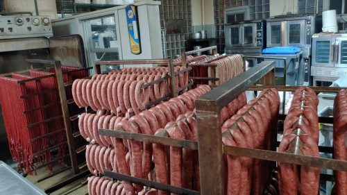 A meat processing room with racks of sausages hanging and various kitchen equipment in the background.