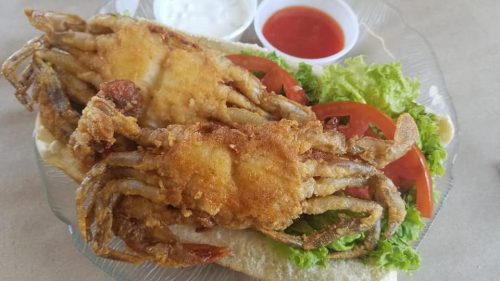 Fried soft-shell crabs on a bun, served with lettuce, tomato, and dipping sauces on the side.