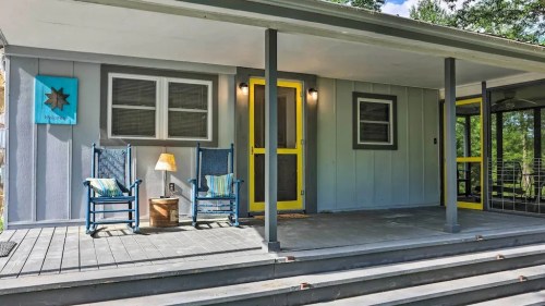 A cozy porch with yellow accents, rocking chairs, and a lamp, surrounded by greenery and blue skies.