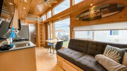 Cozy interior of a beach-themed cabin with wooden walls, a sofa, and large windows letting in natural light.