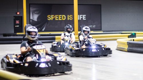 Three go-karts racing on an indoor track, with a "SPEED IS LIFE" sign in the background.