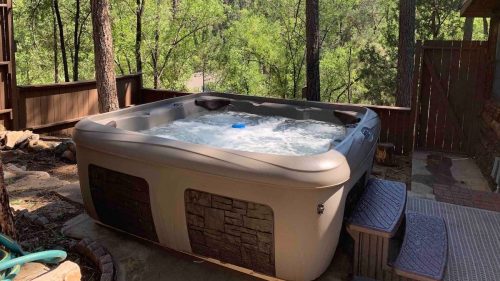 A hot tub surrounded by trees and a wooden deck, creating a serene outdoor relaxation space.