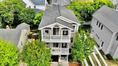 Aerial view of a large, multi-story house surrounded by trees and other homes, featuring a driveway and balconies.