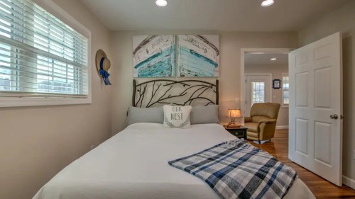 Cozy bedroom with a bed, decorative wall art, a throw blanket, and a chair, featuring soft lighting and neutral colors.