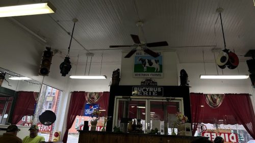 Interior of a shop with a ceiling fan, red curtains, and a sign for Whitman Farms on the wall.
