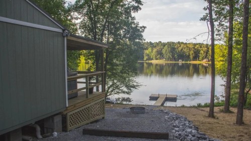 A serene lakeside view with a cabin, dock, and trees reflecting in the calm water.