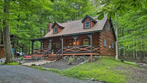 A charming log cabin surrounded by lush green trees, featuring a porch and stone pathway.