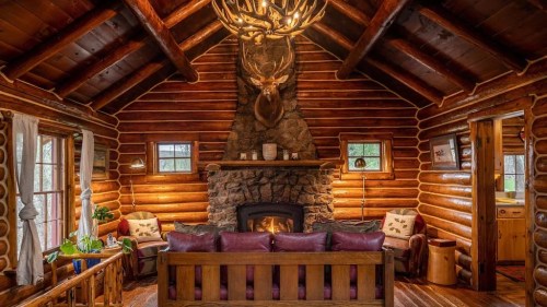 Cozy log cabin interior with a stone fireplace, wooden beams, and rustic decor, featuring a warm, inviting atmosphere.