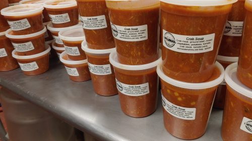 Containers of crab soup lined up on a kitchen counter, each labeled with ingredients and storage instructions.
