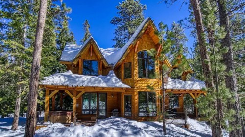 A cozy wooden cabin surrounded by snow-covered trees under a clear blue sky.